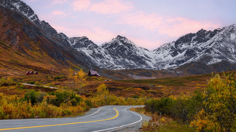 Winding road through snowy mountains with red buildings and cabins in Alaska