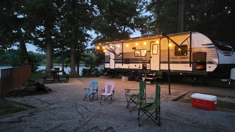 Trailer parked at a wooded waterfront campsite with several folding chairs and a string lights illuminating the place at the Mississippi River State Park campground, Arkansas