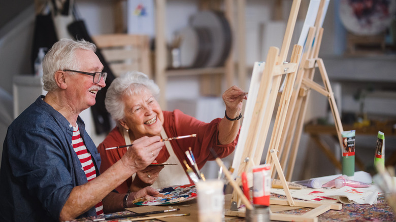 An elderly couple painting on canvas