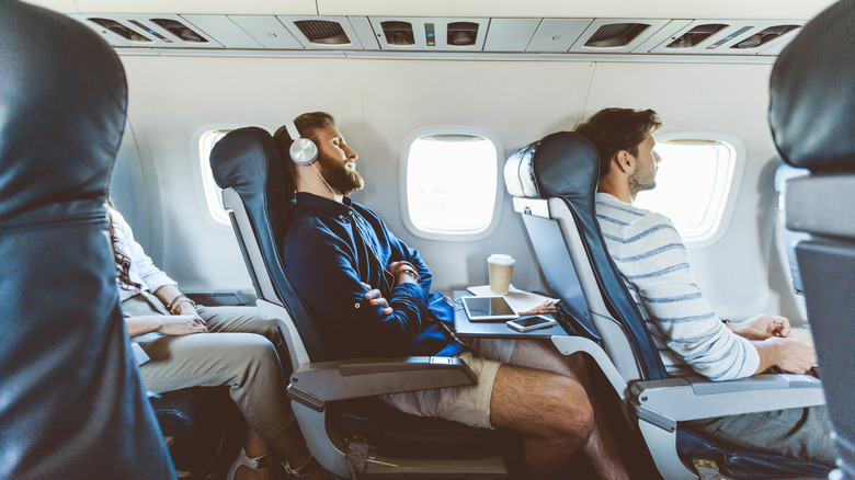 A bearded man sleeping on a plane with headphones on