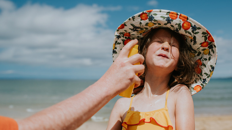 A child in an oversized hat, having sunscreen applied