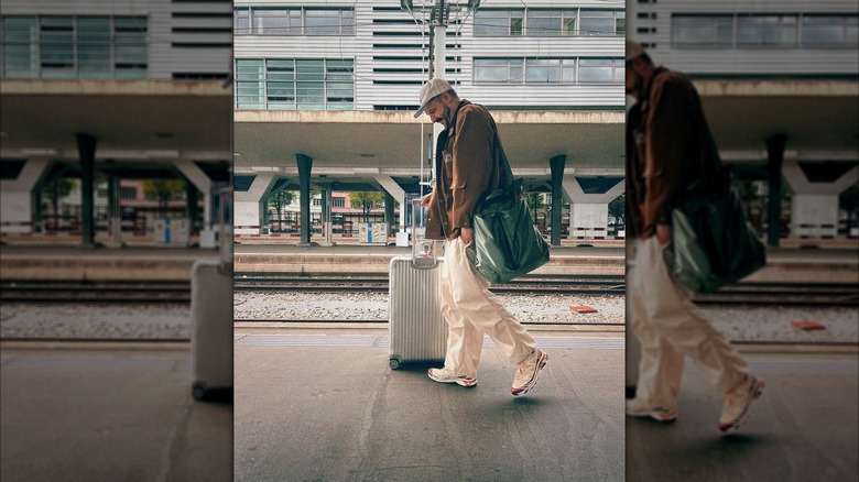 A man walks along a train platform with a Rimowa suitcase