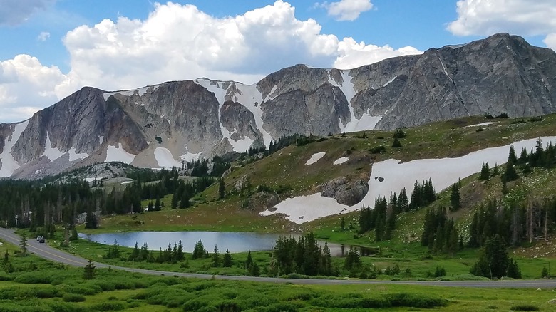 A pristine view of a small lake surrounded by copses of trees and a vast mountain