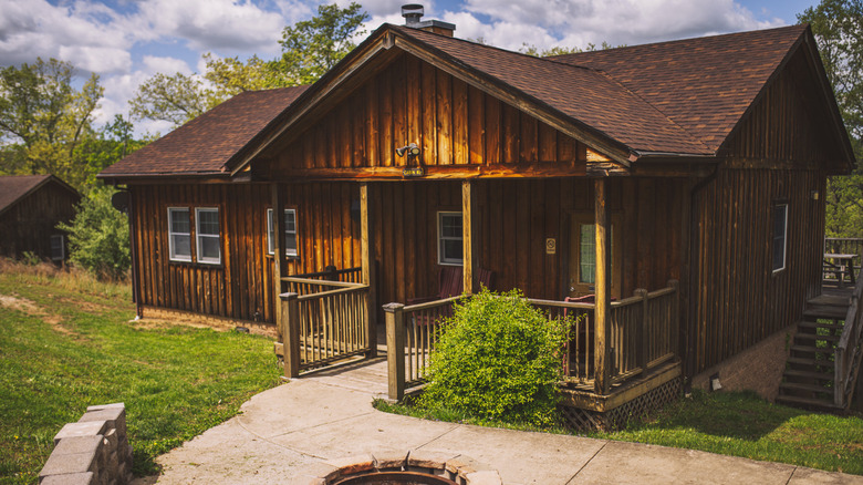 brown cabin with concrete walkway and green trees in back