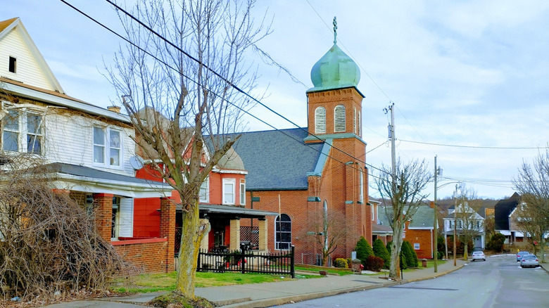 Street lined in winter trees with white home, red home, and red-brick church topped with green dome.