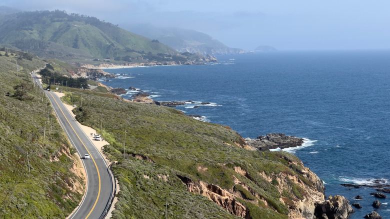 A car drives a highway beside a rocky coastline