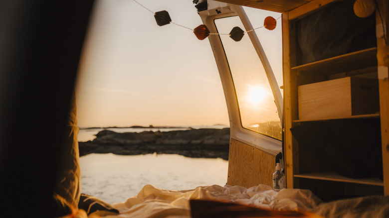 View of the beach from inside a camper van with blankets and fairy lights.