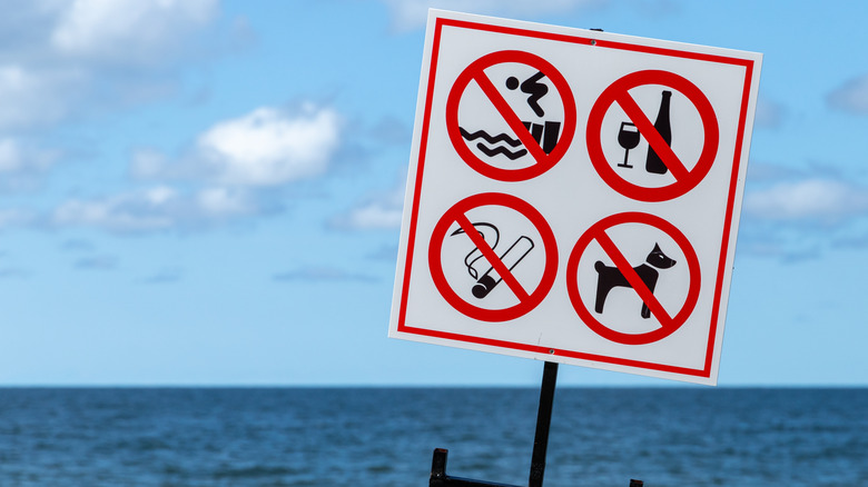 Beach rules icons on a white banner mounted on an ocean beach.