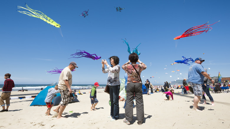 Festival goers take photos and walk along beach as kites soar overhead during the Lincoln City, Oregon kite festival