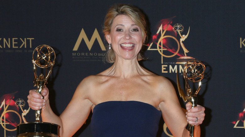 Samantha Brown smiling and holding two Emmy awards on the red carpet