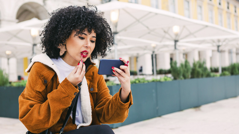 Woman applying red lip gloss in front of hotel