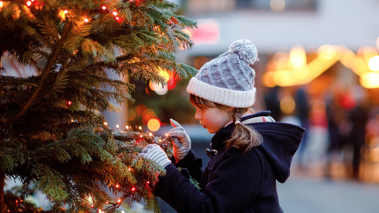 young girl in hat and coat looking at a Christmas tree