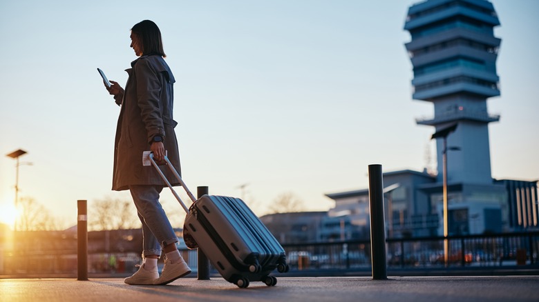 A woman walking while rolling a carry-on luggage outside