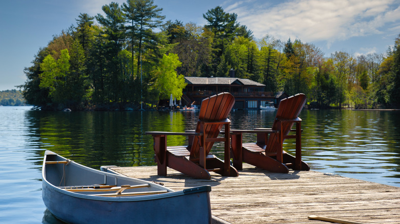 Two wooden chairs on a pier next to a kayak in a rural lake