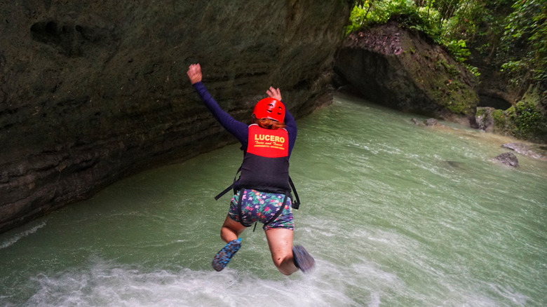 Woman wearing helmet and life jacket jumping into river while canyoneering.