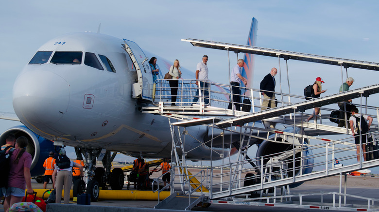 A line of passengers exit an Allegiant airbus via a shaded ramp leading out from the front left door of the aircraft