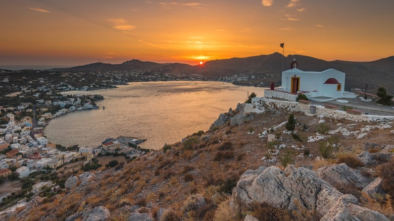 Sunset over a bay with a white chapel on a rocky hill overlooking the water and town belowl