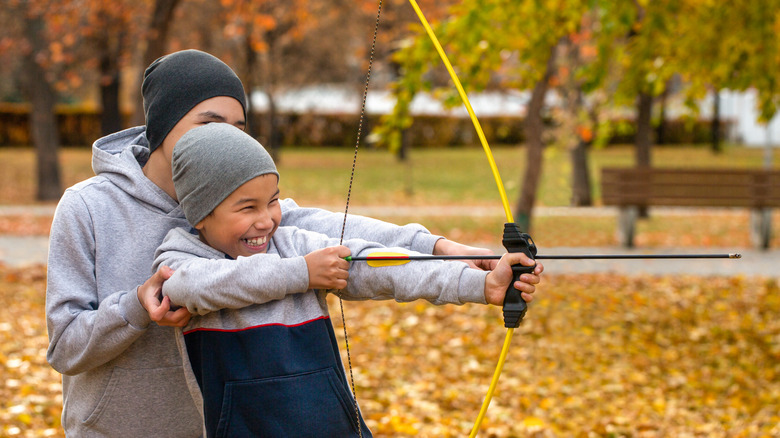 Man helping a boy use a bow and arrow during fall
