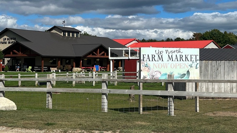 A large billboard-style sign in front of Up North Farm Market reveals the market is now open