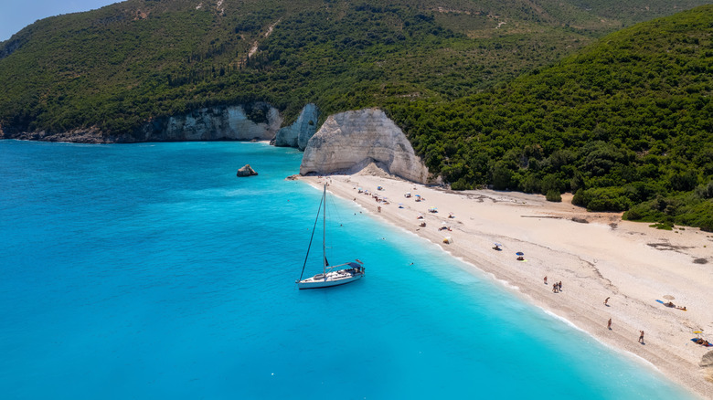Cliffs of white stone topped by lush greenery descent to meet white pebbles and blue seas