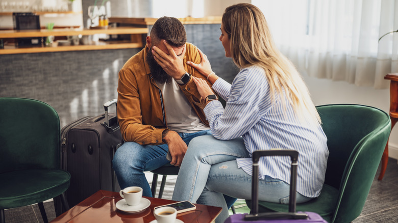 A woman comforts her frustrated husband in a hotel lobby.