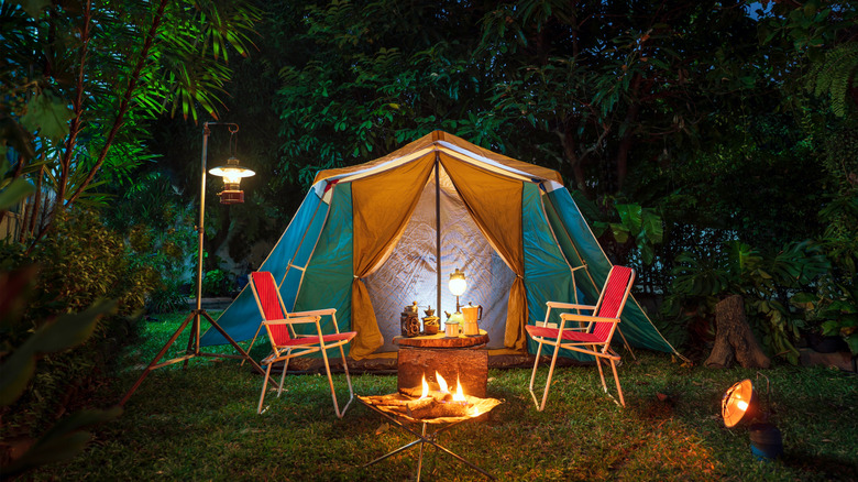 Campsite at night with a tent, chairs, and lights