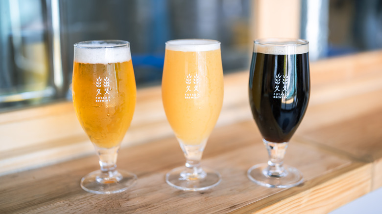 Three glasses filled with craft beers of different shades (amber, creamy amber, and dark black)