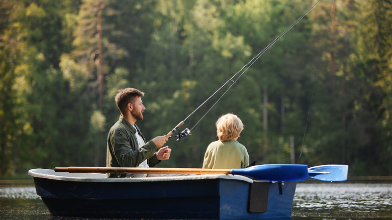 A man and a boy fish from atop a boat in the middle of a lake