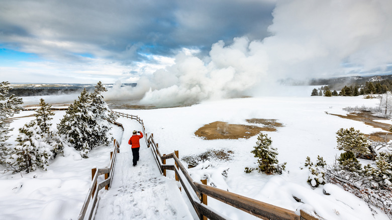 Person hiking along a snowy trail by a geyser in winter, Yellowstone National Park