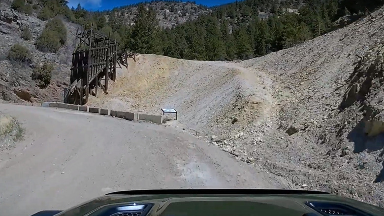 A vehicle driving down the Oh My God Road with old mining structures in the background