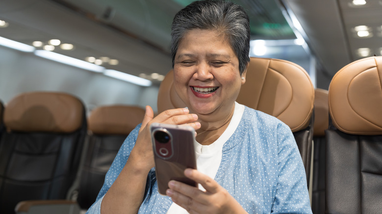 An elderly woman using her mobile phone on a flight.