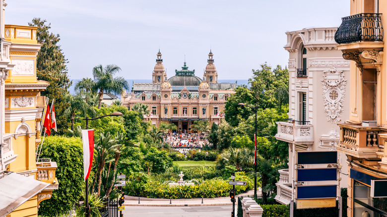 Facade of the Monte Carlo Casino with lush gardens in the front and the flag of Monaco hanging