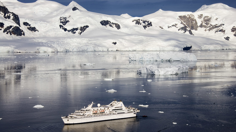 A cruise ship in Antarctica surrounded by snow-covered mountains and icebergs in the water.