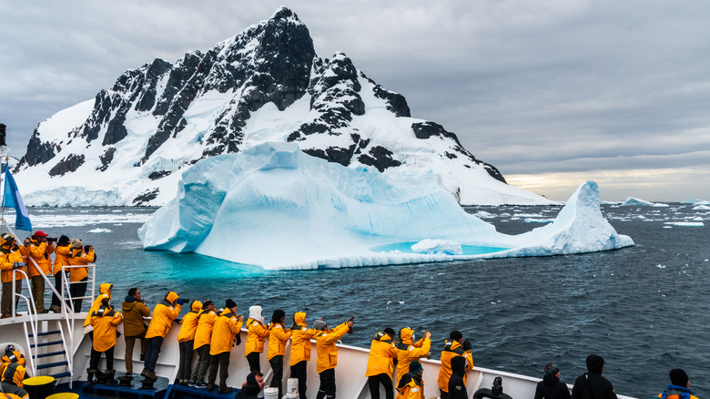 Tourists aboard an Antarctica cruise ship crowd on one side while looking at an iceberg.