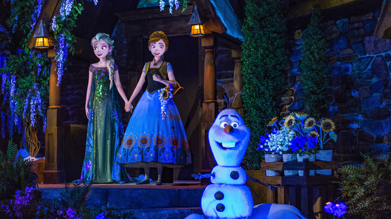 A scene of Ana and Elsa holding hands with Olaf in the foreground.