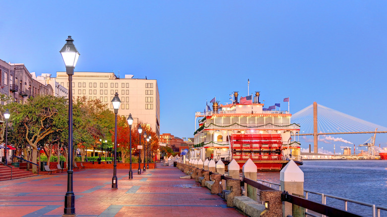 The boardwalk in Savannah, Georgia, lined with lamp posts and a large boat docked in the water
