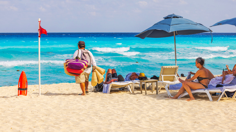 A beach vendor in Cancun carries straw hats to sell to tourists in sun loungers