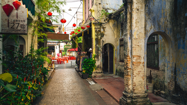 Narrow lane of crumbling brick buildings with red lanterns and red cafe chairs