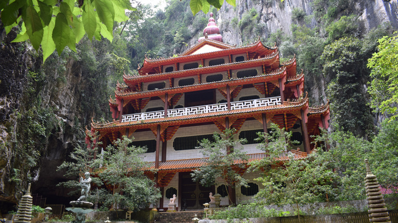 Giant pagoda with red shingles built into a cliff thick with jungle vegetation