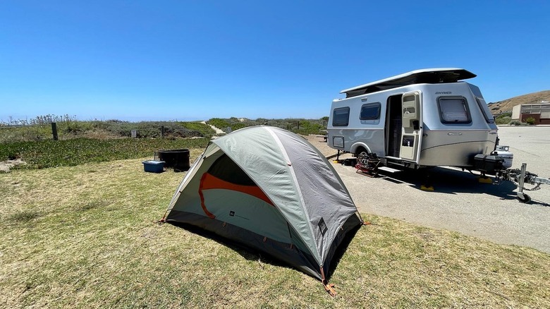 A small tent and silver trailer in front of the dunes at Morro Strand State Beach, California.
