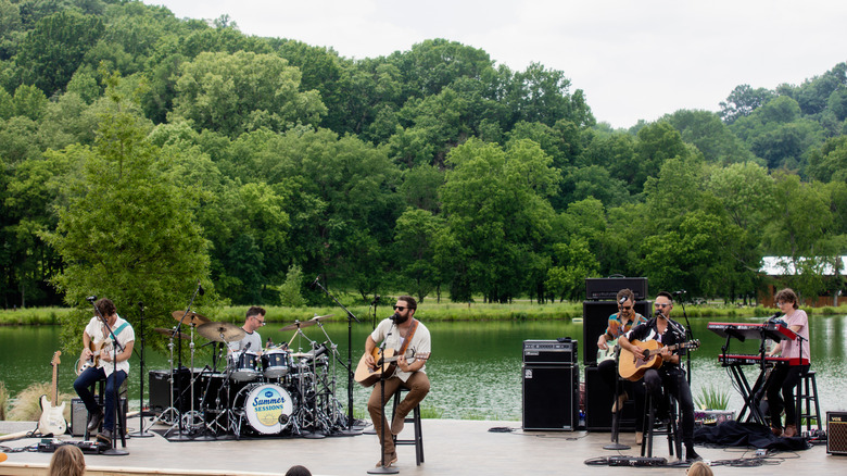 A band performing on stage with a lake and trees in the background at Southall Farm & Inn.