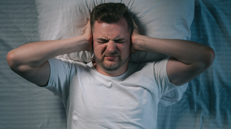 Guy laying in a bed covering ears to block noise