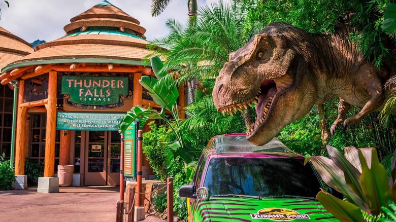 Exterior view of Thunder Falls Terrace, a quick-service restaurant inside the Jurassic Park land of Islands of Adventure, one of the theme parks that make up Universal Orlando Resort in Florida, USA, pictured along with a T-rex replica and a prop car from the film series in the foreground