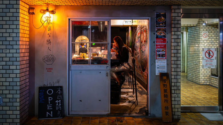 Woman eating ramen in a small ramen kiosk