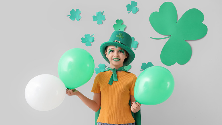 A child holding green balloons and wearing green face art