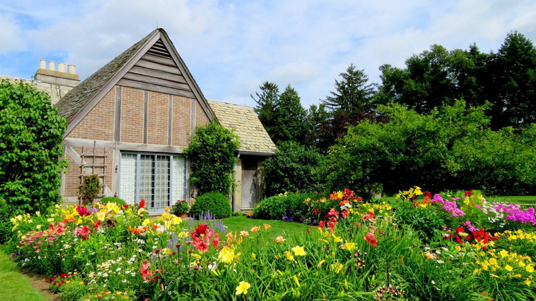 The historic Tudor house at Topsmead State Forest in Torrington, Connecticut, surrounded by green trees, a blue sky, and colorful flowers.