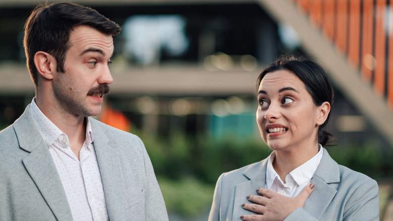 Man and woman in business casual attire exchanging a visibly uncomfortable conversation outside a modern office building