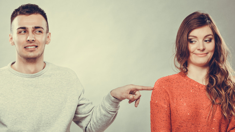 Shy woman and man sitting on sofa couch next each other. the man is touching the woman's shoulder with one finger.