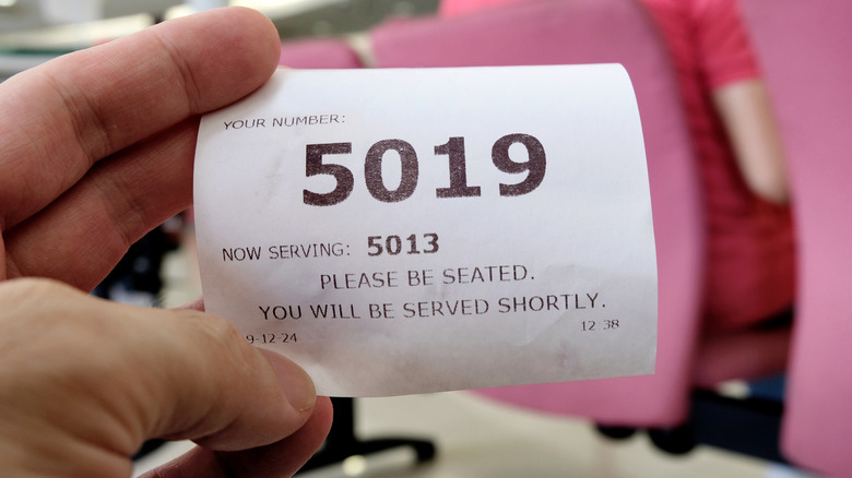 Hand holding a queue number ticket for a counter service at a bank while waiting turn to be attended to
