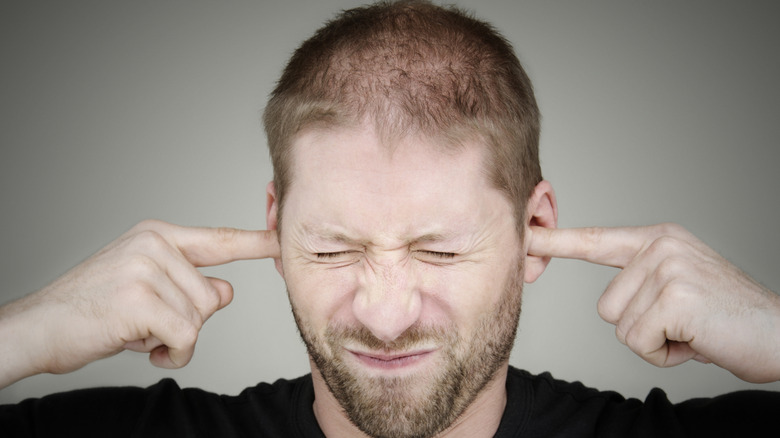 Man with finger in his ears and eyes screwed up tight